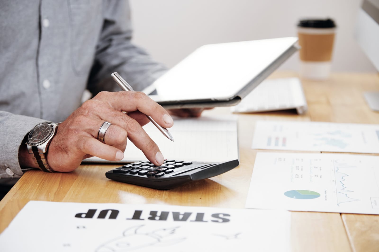 Pessoa fazendo cálculo financeiro com calculadora, tablet e gráficos sobre a mesa