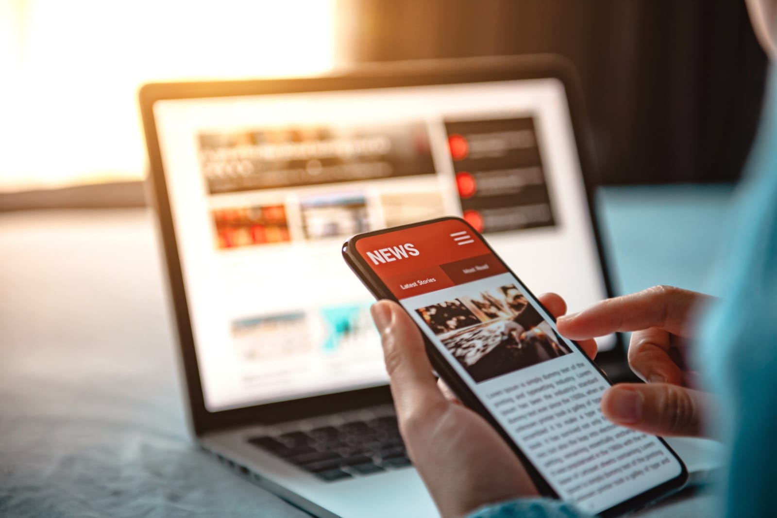 Pessoa consultando notícias e avaliações pelo celular, com laptop ao fundo