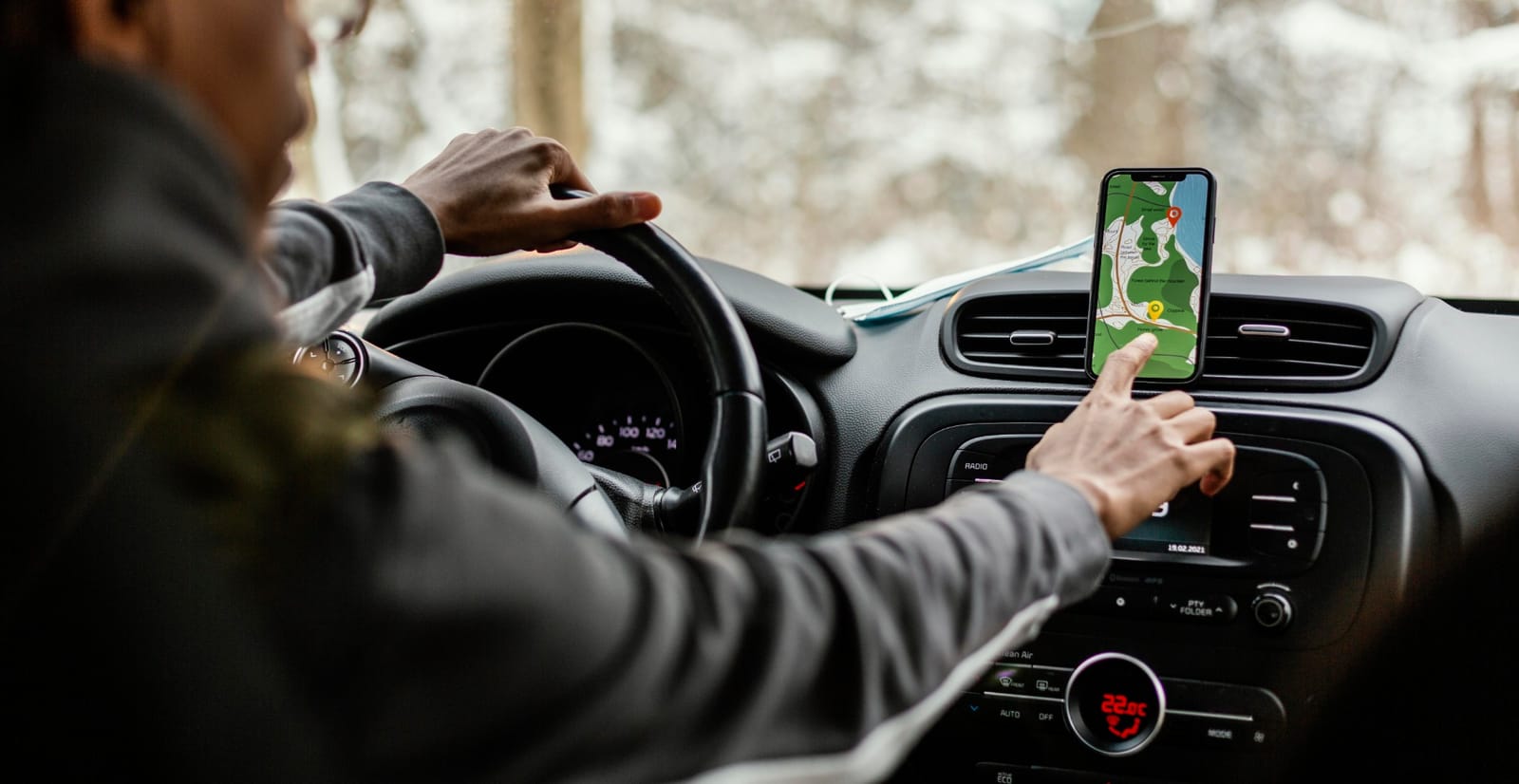 Pessoa dirigindo um carro com o celular preso ao painel mostrando um aplicativo de navegação