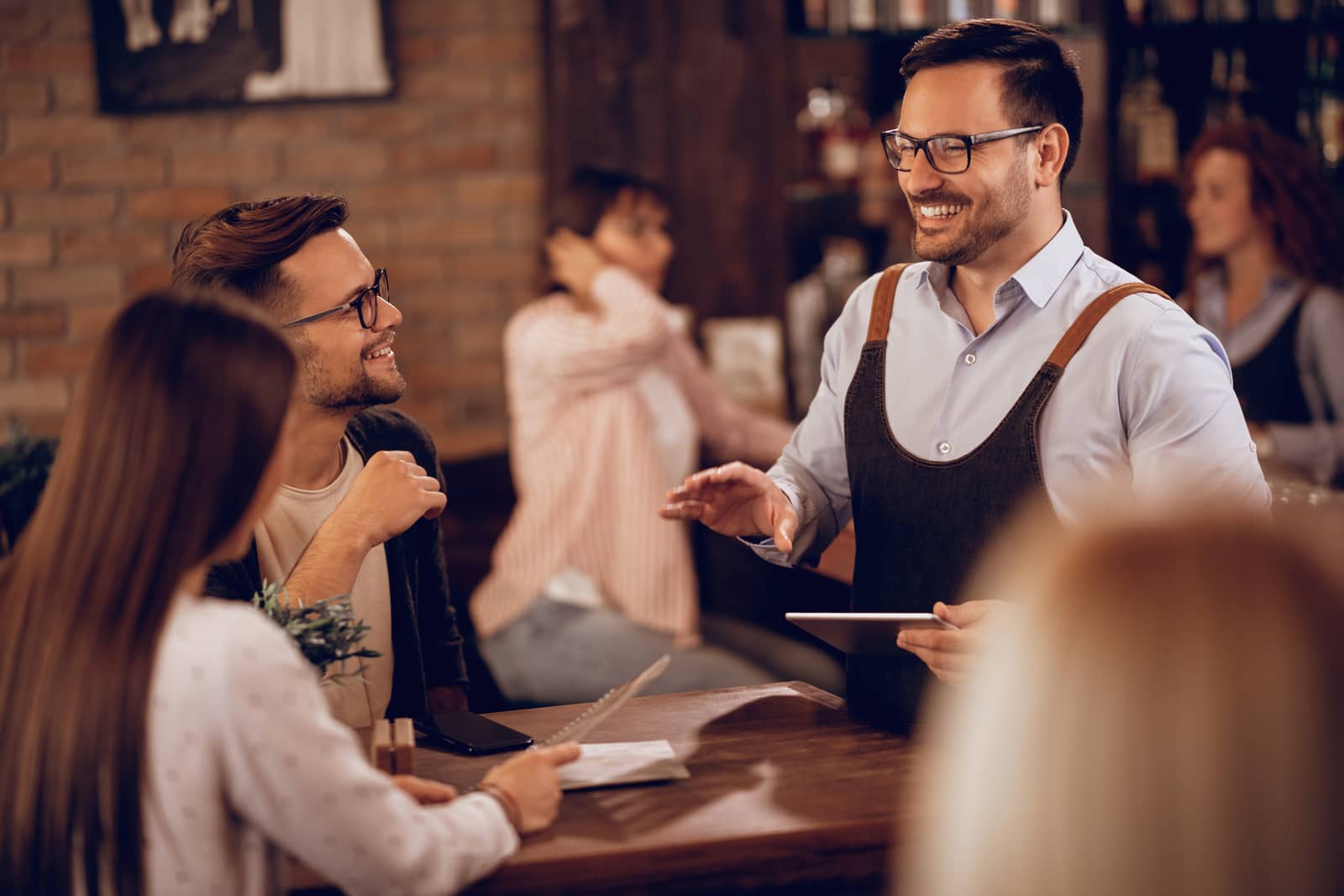 Garçom sorridente com um tablet conversando com clientes no balcão de um restaurante